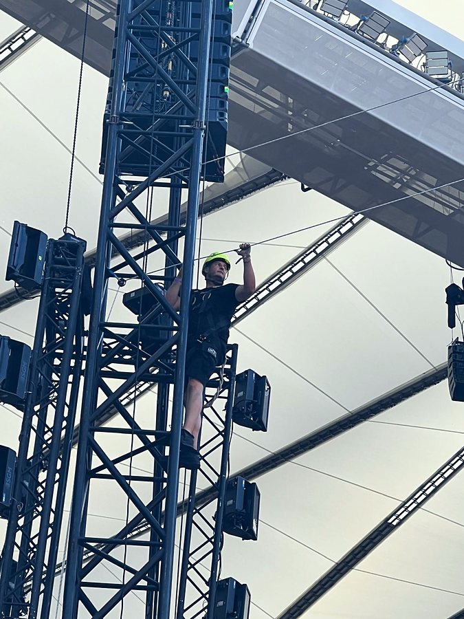 Montador de Linecam con casco y arnés tensando la cuerda del cablecam en una torre de sonido