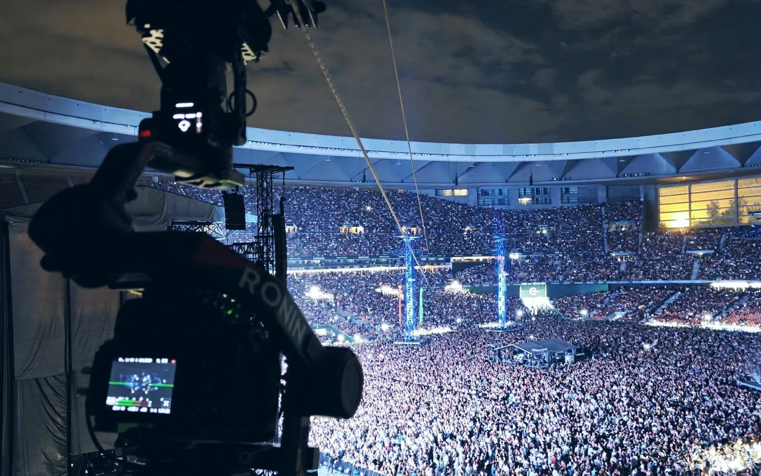 Linecam cablecam crossing a packed stadium during a concert, seen from the stands