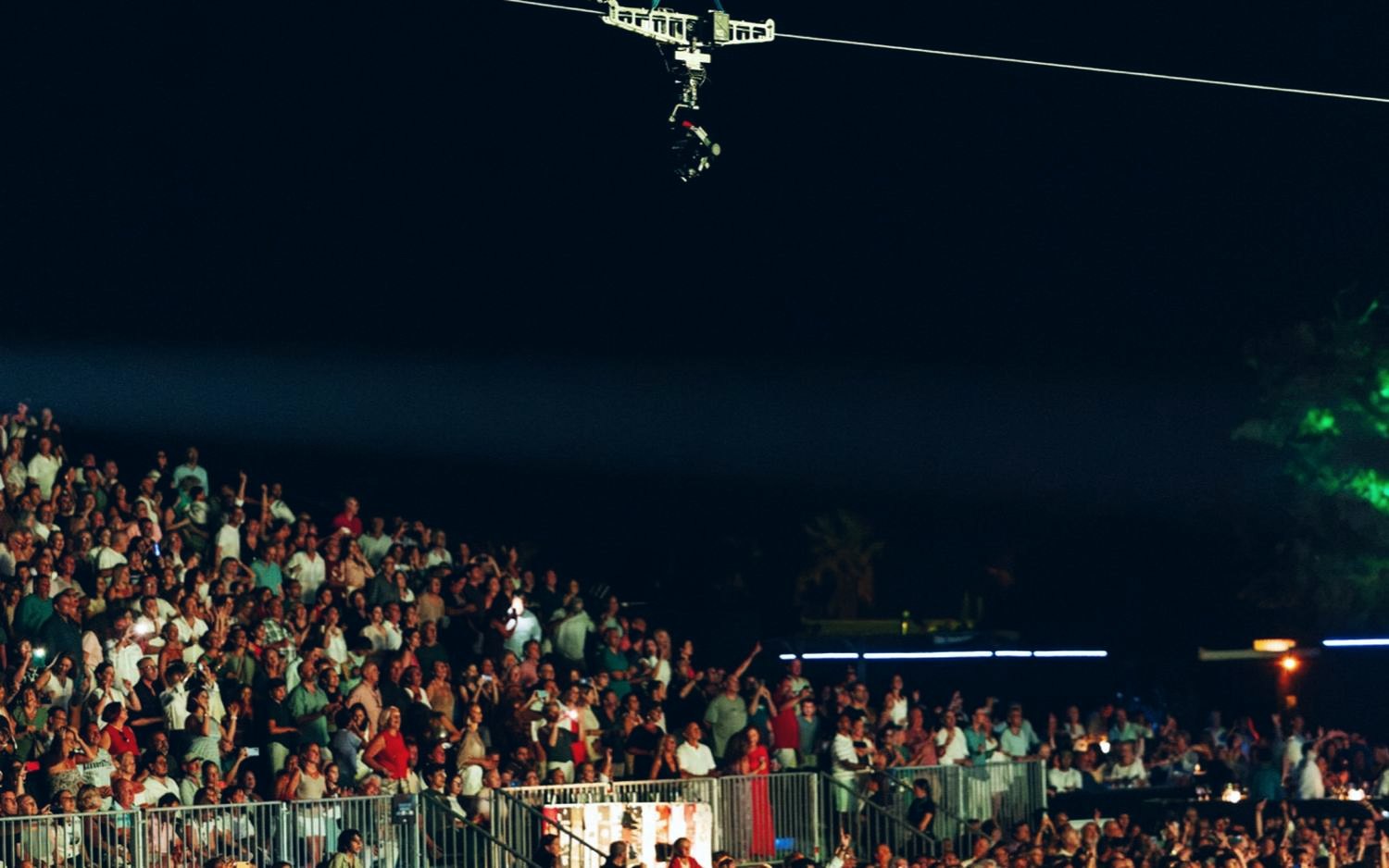 Linecam cablecam crossing above the crowd at a night concert with stage lights